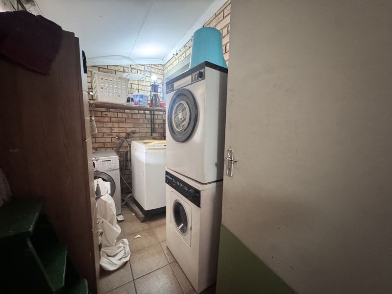A functional laundry area featuring exposed brick walls, tiled flooring, and dedicated plumbing connections for washing machines and dryer units.