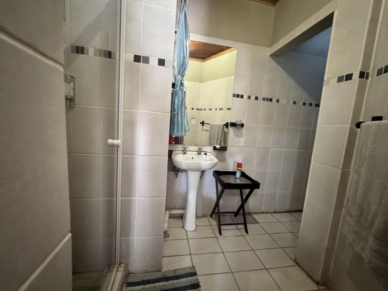 A functional bathroom featuring a pedestal basin, shower enclosure, and neutral wall tiling with decorative accents.