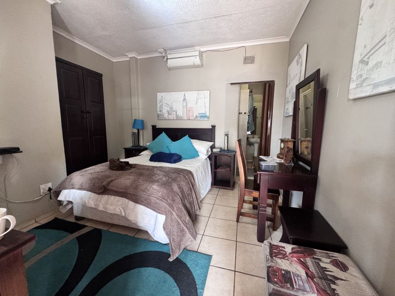 A functional bedroom featuring tiled flooring, a built-in wardrobe, and an en-suite bathroom, equipped with a wall-mounted air conditioning unit.