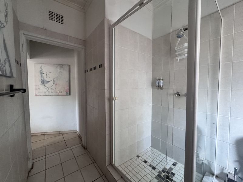 A functional bathroom featuring a glass-enclosed shower with neutral ceramic wall and floor tiling.