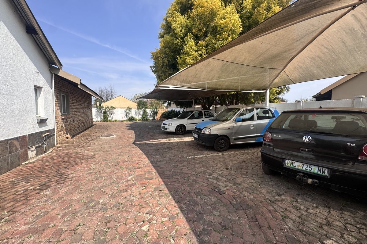 Rear exterior area featuring a paved driveway and a large shade cloth carport structure for vehicle parking.