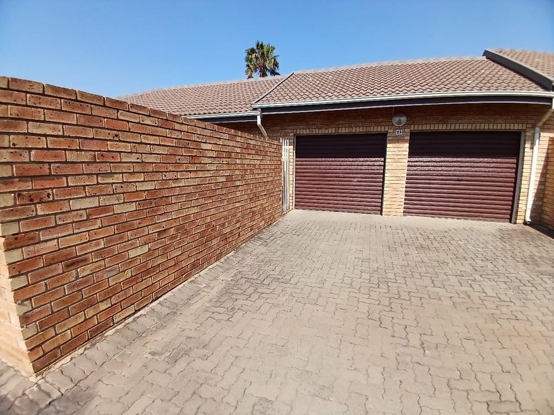 A double garage with roller doors and a paved driveway, featuring a brick boundary wall and tiled roof.