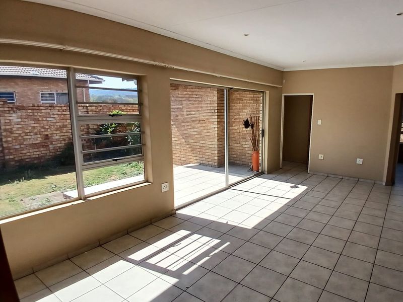 Spacious, empty living area featuring tiled flooring, large sliding glass doors leading to a patio, and louvered windows providing natural light.