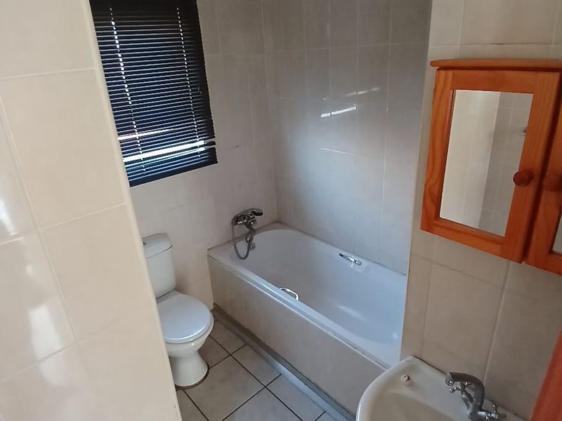 A functional bathroom featuring a bathtub, pedestal basin, and toilet with neutral wall and floor tiling.
