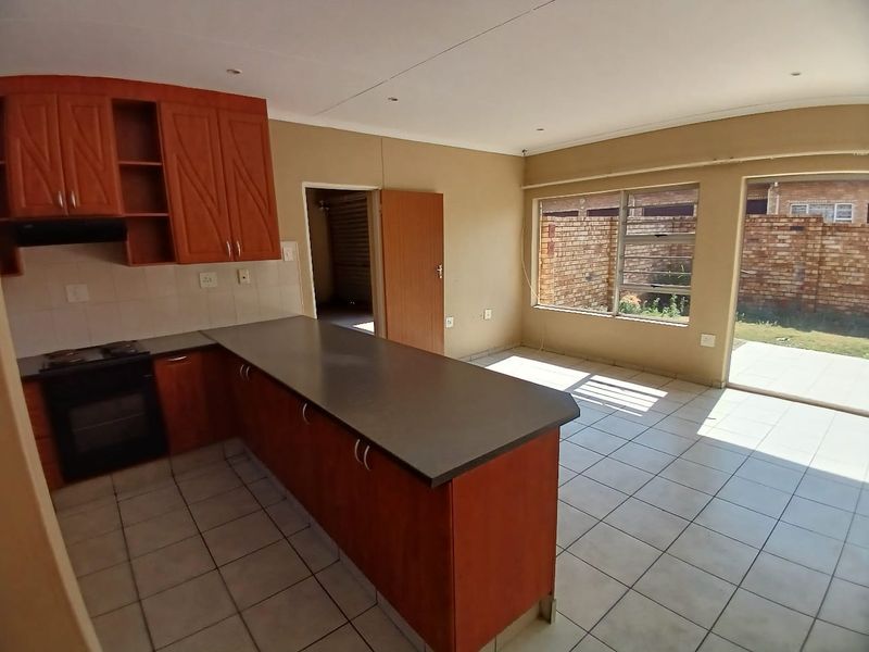 Open-plan kitchen and living area featuring tiled flooring, built-in cabinetry with laminate countertops, and direct access to the rear patio through a sliding door.