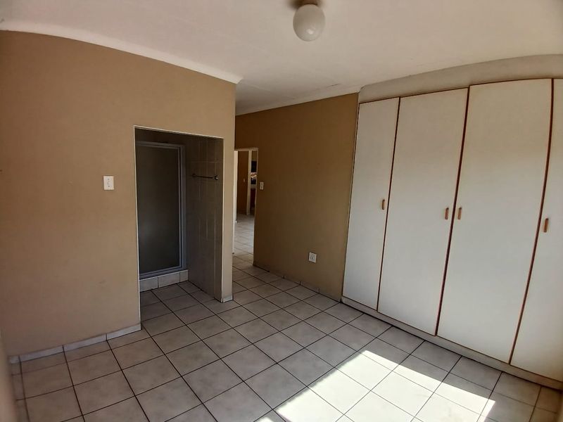 An empty bedroom featuring built-in cupboards, tiled flooring, and an en-suite shower area, offering a functional space ready for personalization.