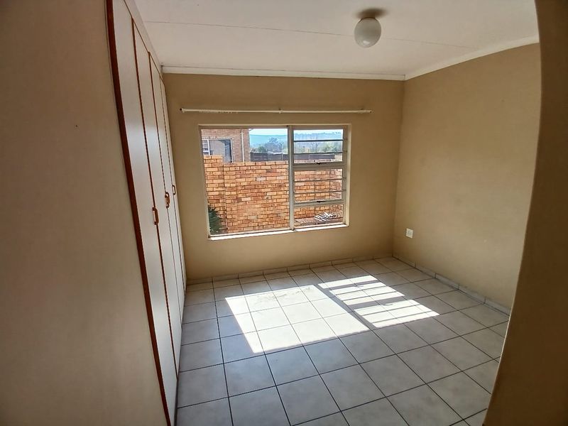 A vacant bedroom featuring tiled flooring, built-in cupboards, and a window with views of the exterior brick wall.