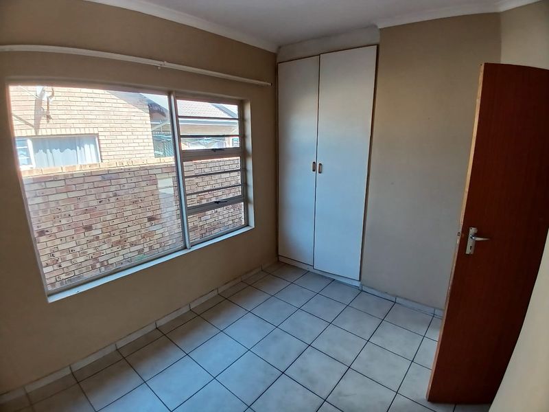 A vacant bedroom featuring tiled flooring, a built-in wardrobe, and large windows providing natural light.