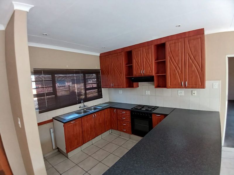A functional kitchen featuring wood-finish cabinetry, dark laminate countertops, a built-in oven with hob, and tiled flooring, offering a clean and practical workspace.