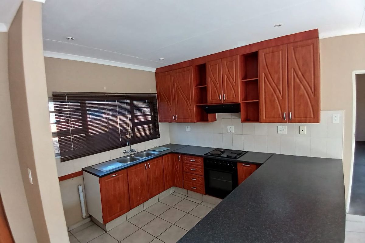 A functional kitchen featuring wood-finish cabinetry, dark laminate countertops, a built-in oven with hob, and tiled flooring, offering a clean and practical workspace.