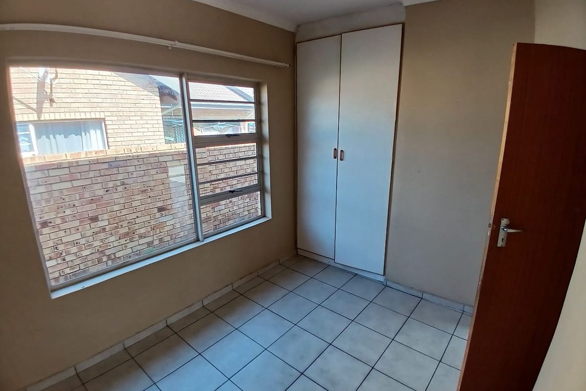 A vacant bedroom featuring tiled flooring, a built-in wardrobe, and large windows providing natural light.