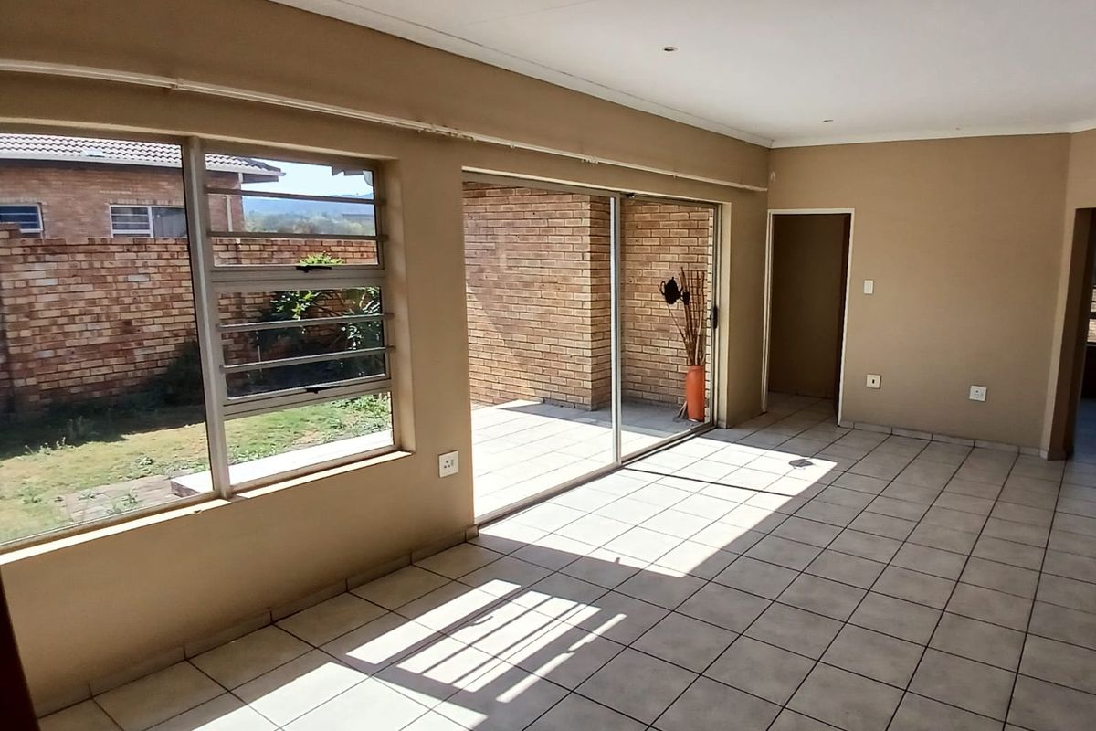 Spacious, empty living area featuring tiled flooring, large sliding glass doors leading to a patio, and louvered windows providing natural light.