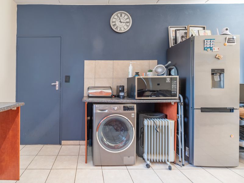 A functional kitchen area featuring tiled flooring, a tiled backsplash, and a laminate countertop with space for laundry and kitchen appliances.
