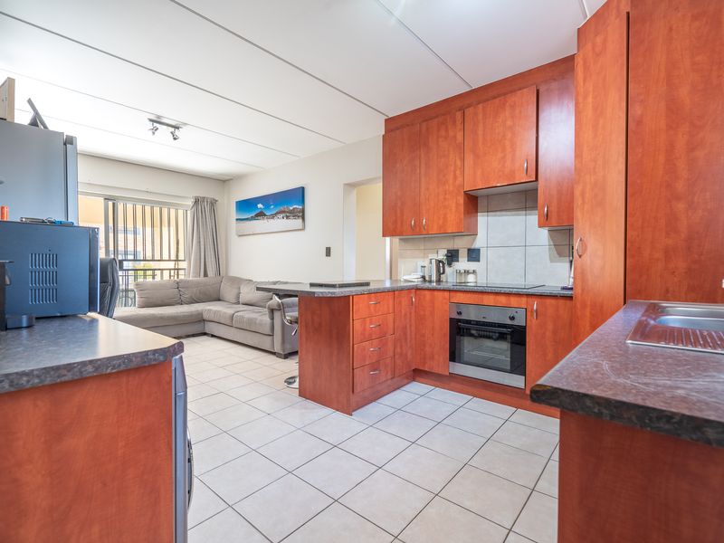 Open-plan kitchen and living area featuring wood-finish cabinetry, tiled flooring, and direct access to a balcony through a sliding glass door.
