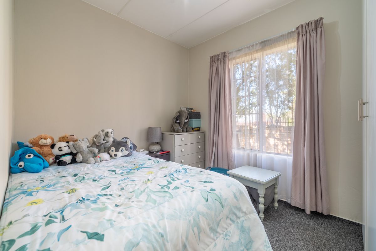 A cozy bedroom featuring neutral wall tones, carpeted flooring, and a built-in cupboard, providing a functional and comfortable living space.