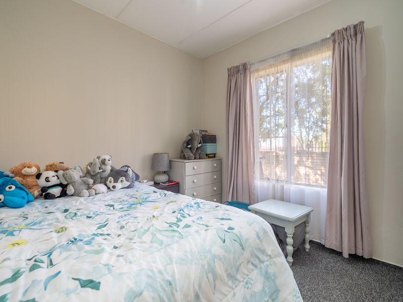 A cozy bedroom featuring neutral wall tones, carpeted flooring, and a built-in cupboard, providing a functional and comfortable living space.