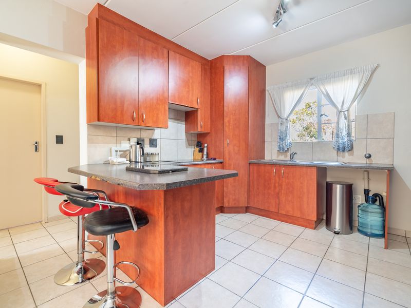 A functional kitchen featuring wood-look laminate cabinetry, tiled flooring, a breakfast bar, and a tiled backsplash with a built-in sink area.