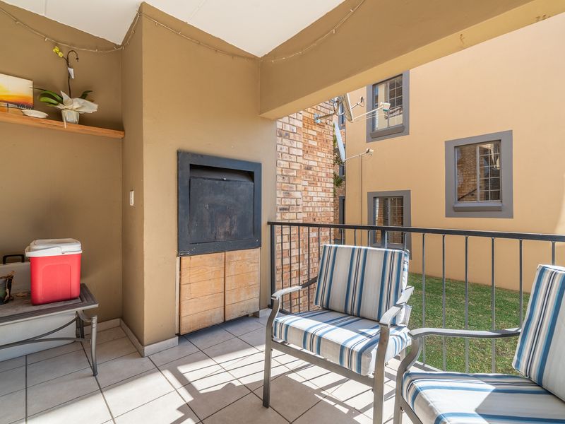 Covered balcony featuring a built-in braai, tiled flooring, and metal railings, overlooking a small communal garden area.