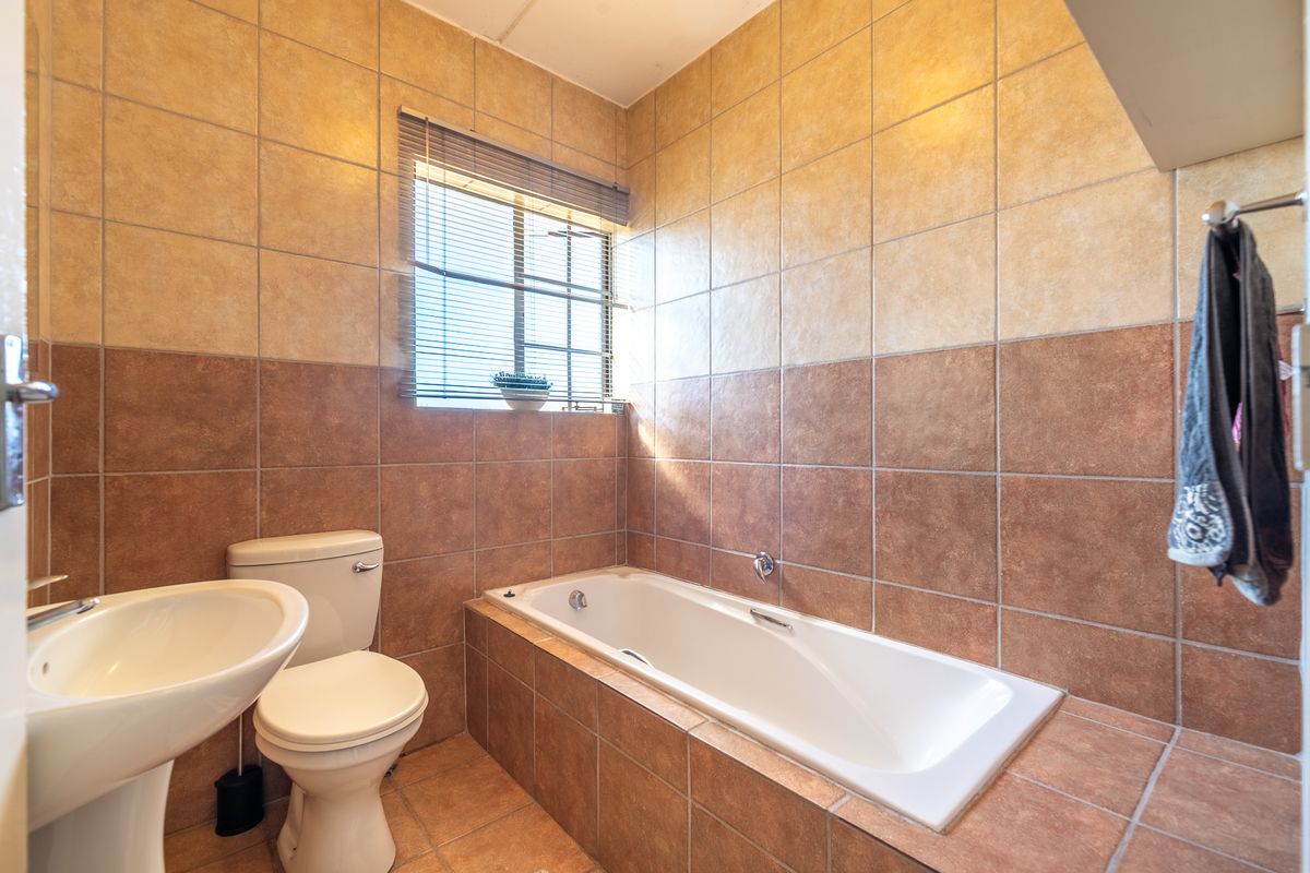 A functional bathroom featuring a built-in bathtub, pedestal washbasin, toilet, and full-height wall tiling with a neutral color palette.
