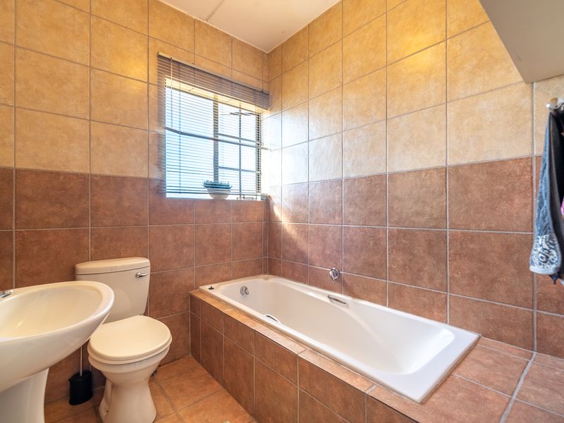 A functional bathroom featuring a built-in bathtub, pedestal washbasin, toilet, and full-height wall tiling with a neutral color palette.