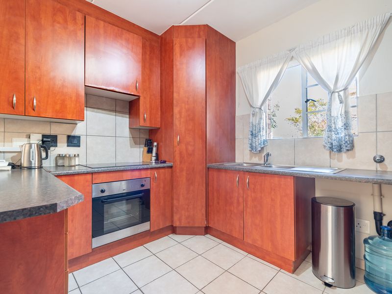 Functional kitchen featuring wood-finish cabinetry, laminate countertops, built-in oven and hob, and tiled backsplash with a window view.