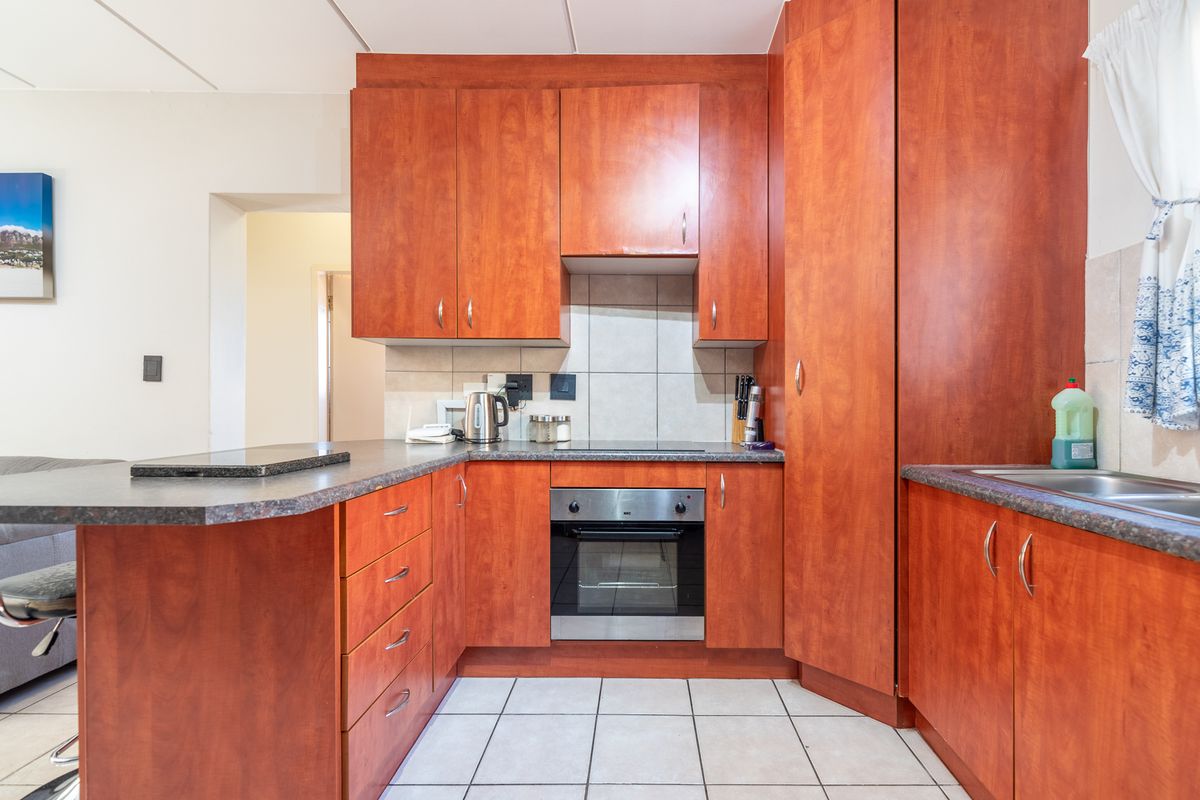 A functional kitchen featuring wood-finish cabinetry, laminate countertops, a built-in electric oven and hob, and tiled flooring.
