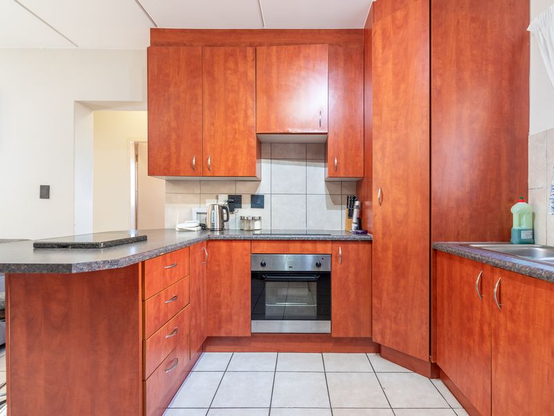 A functional kitchen featuring wood-finish cabinetry, laminate countertops, a built-in electric oven and hob, and tiled flooring.