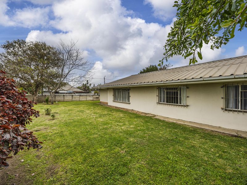 Rear view of the property featuring a metal roof, security bars on windows, and a spacious grass garden with a concrete boundary wall.
