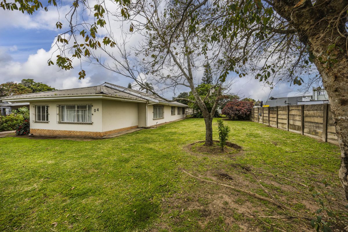 Rear view of the property featuring a spacious lawn, mature trees, and a secure boundary wall with metal window security bars.