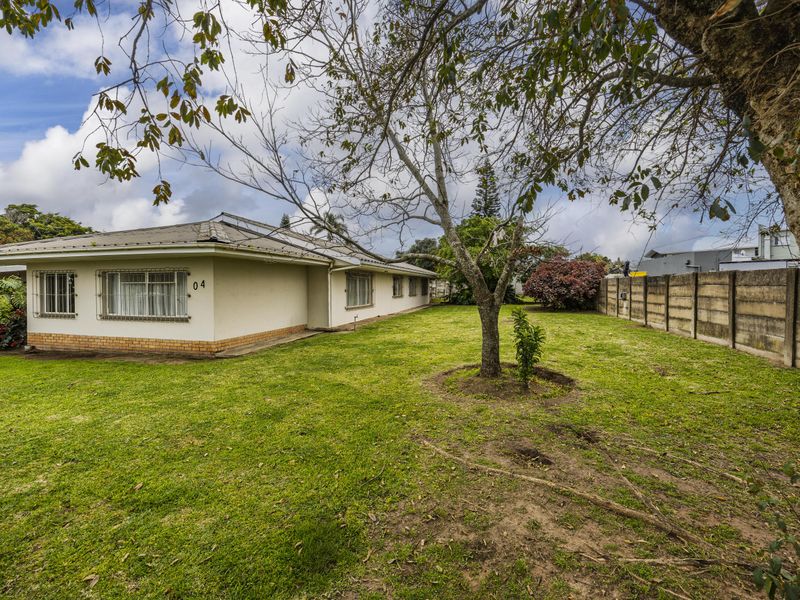 Rear view of the property featuring a spacious lawn, mature trees, and a secure boundary wall with metal window security bars.