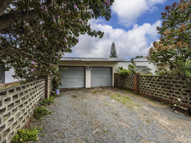 Front exterior view featuring a double garage with roller shutter doors, enclosed by brick boundary walls and a gravel driveway.