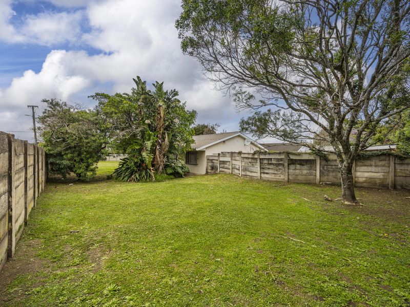 A spacious rear garden featuring a large lawn area, mature trees, and enclosed by precast concrete boundary walls.