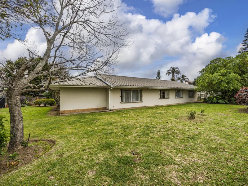 Rear view of the house featuring a metal roof, brick foundation, and a spacious garden area with established trees.