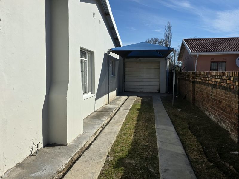 Rear exterior view featuring a garage with a shade sail, concrete driveway strips, and a brick boundary wall.