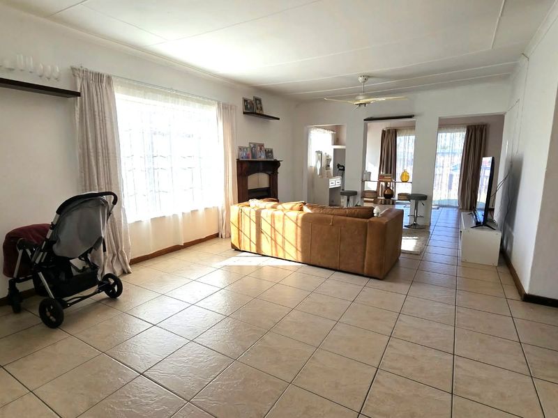 Spacious living room featuring neutral tiled flooring, a ceiling fan, and a fireplace mantel, offering a bright and open layout.