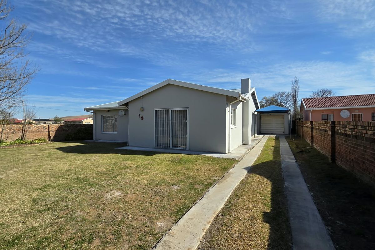 Rear view of the property featuring a spacious lawn, concrete driveway, brick boundary walls, and a detached garage.