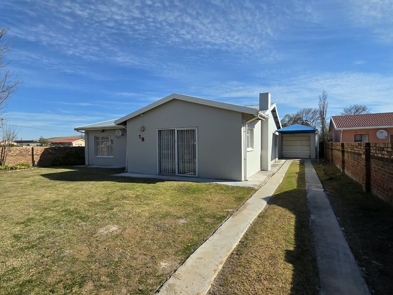 Rear view of the property featuring a spacious lawn, concrete driveway, brick boundary walls, and a detached garage.