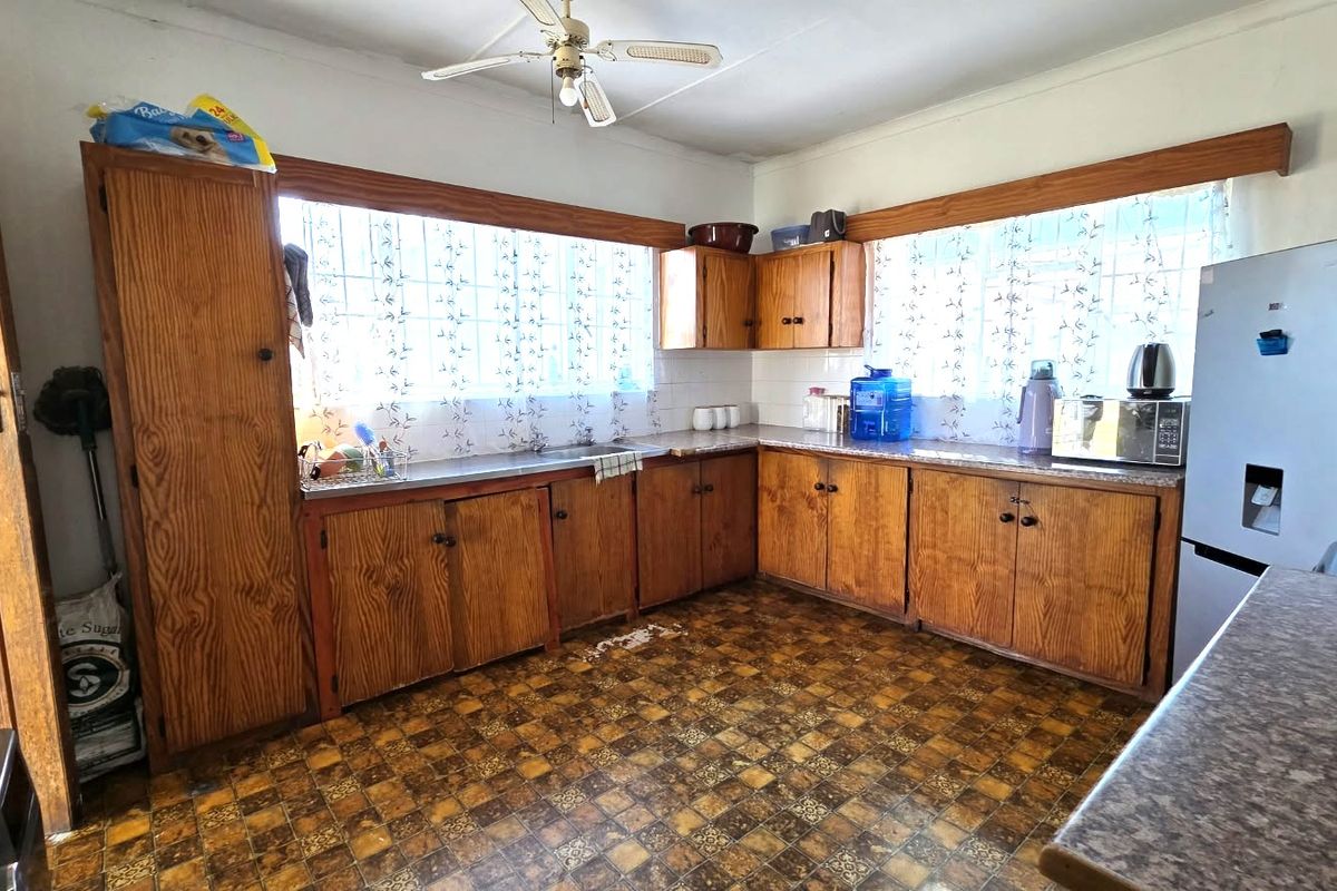 A dated kitchen featuring original wooden cabinetry, laminate countertops, and patterned floor tiles, offering significant potential for a modern renovation.