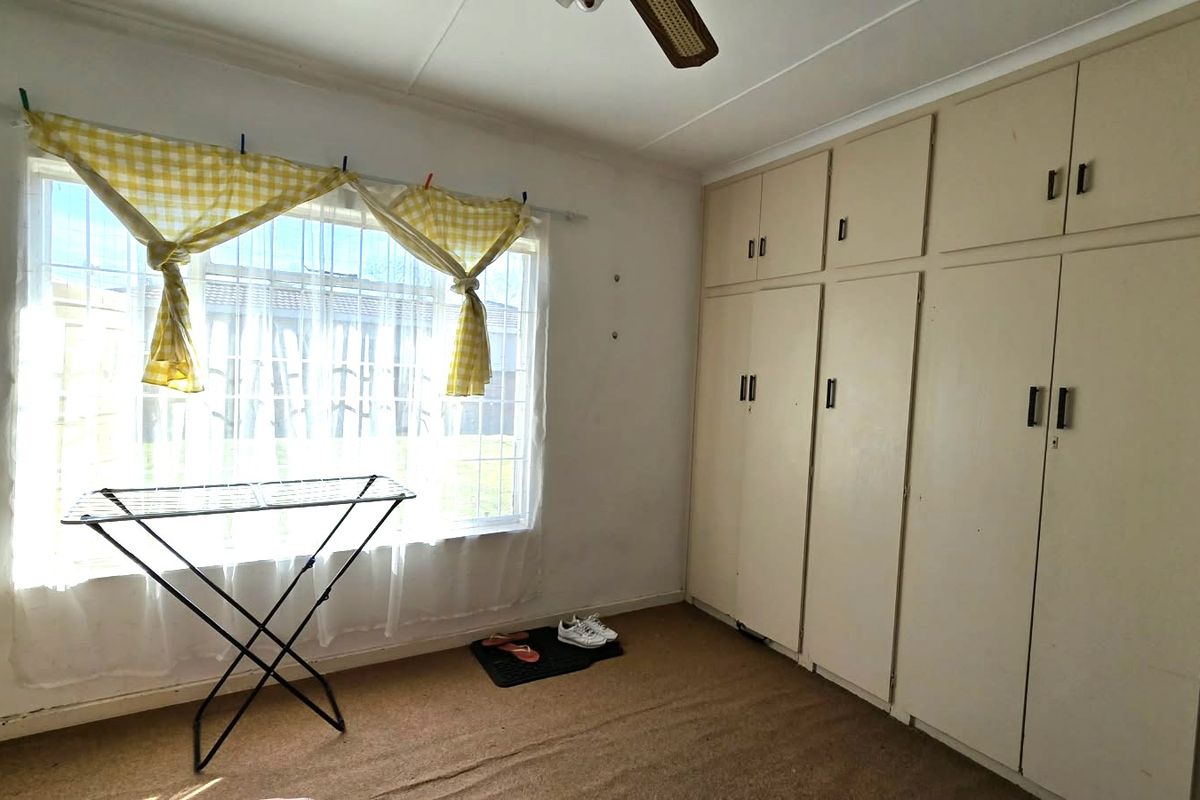 A bedroom featuring built-in cupboards, a ceiling fan, and large windows, offering a blank canvas for renovation and modernization.