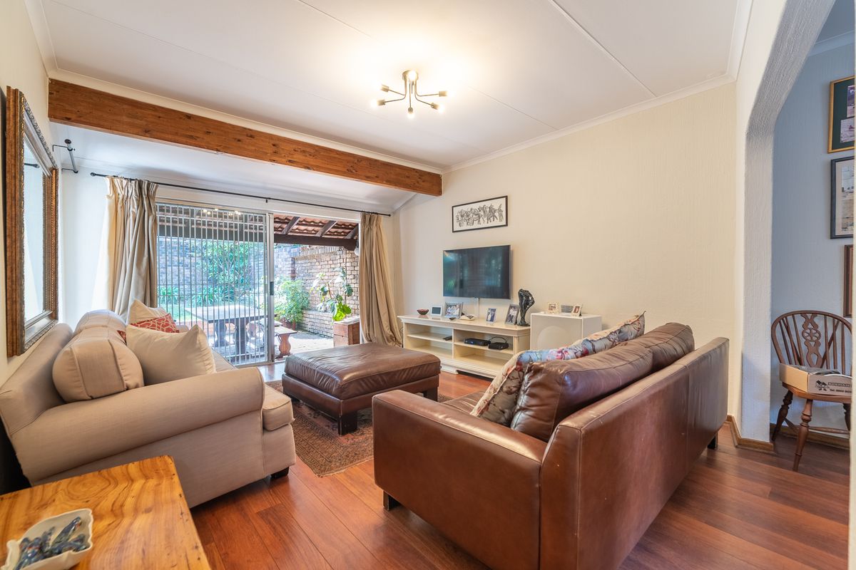 A comfortable living room featuring hardwood flooring, an exposed timber ceiling beam, and direct access to a private patio through sliding glass doors.