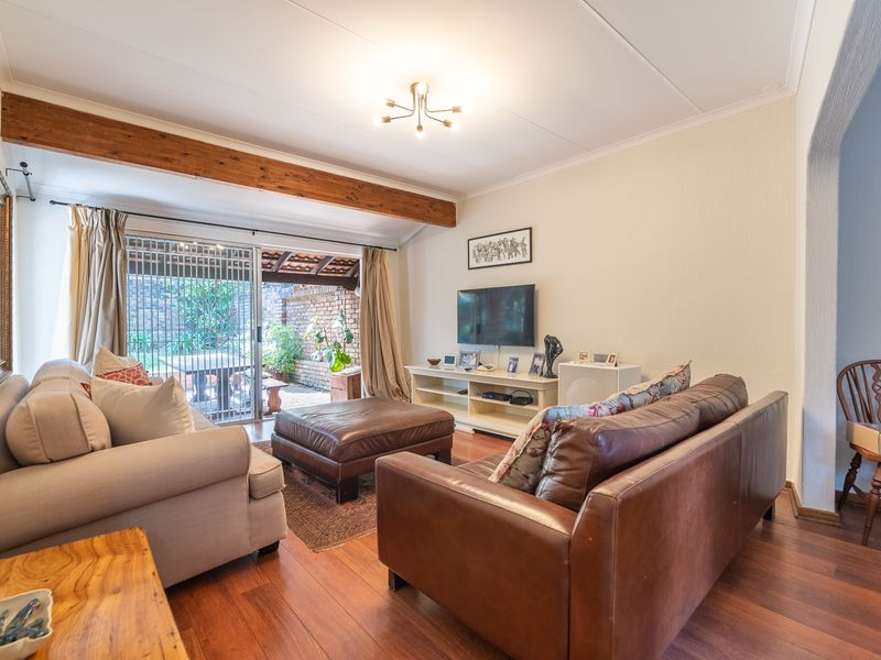 A comfortable living room featuring hardwood flooring, an exposed timber ceiling beam, and direct access to a private patio through sliding glass doors.