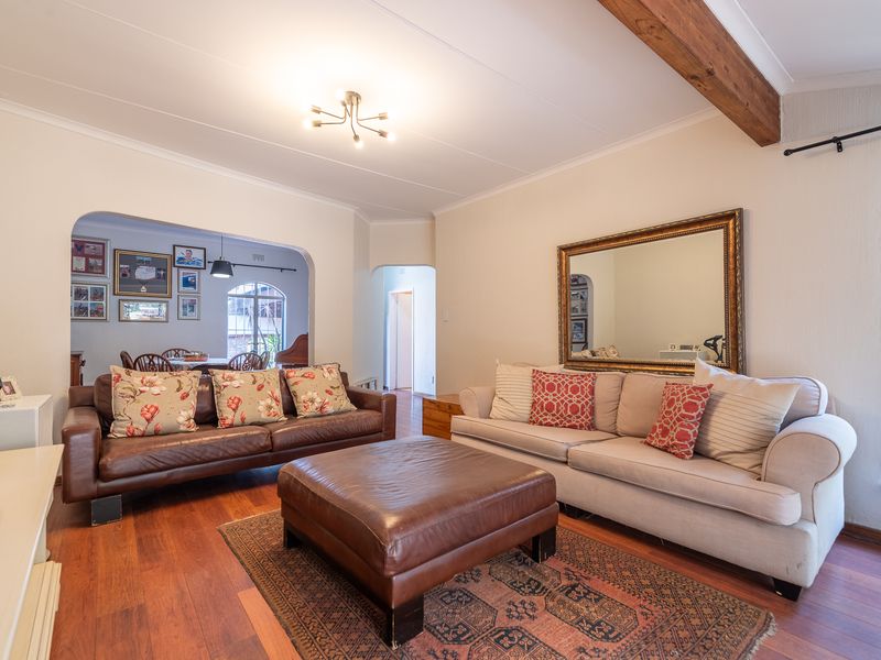 A spacious living room featuring hardwood flooring, an exposed timber ceiling beam, and an arched doorway leading to an adjacent dining area.