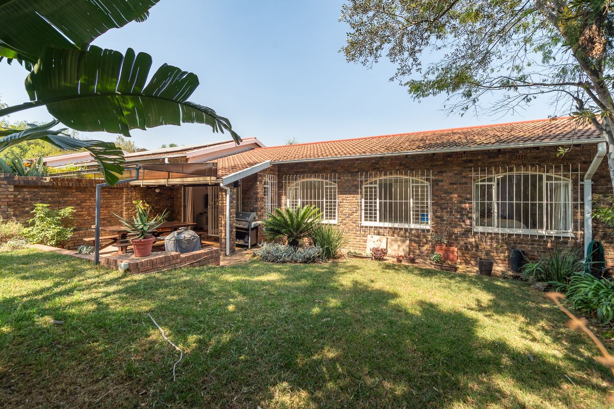 Rear view of the townhouse featuring a brick facade, tiled roof, security bars on windows, and a covered patio area overlooking a private lawn.