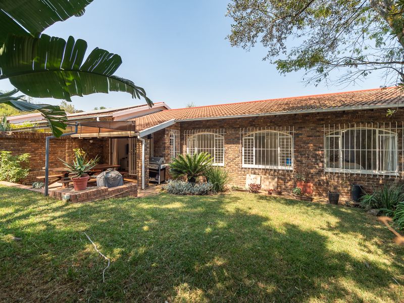 Rear view of the townhouse featuring a brick facade, tiled roof, security bars on windows, and a covered patio area overlooking a private lawn.
