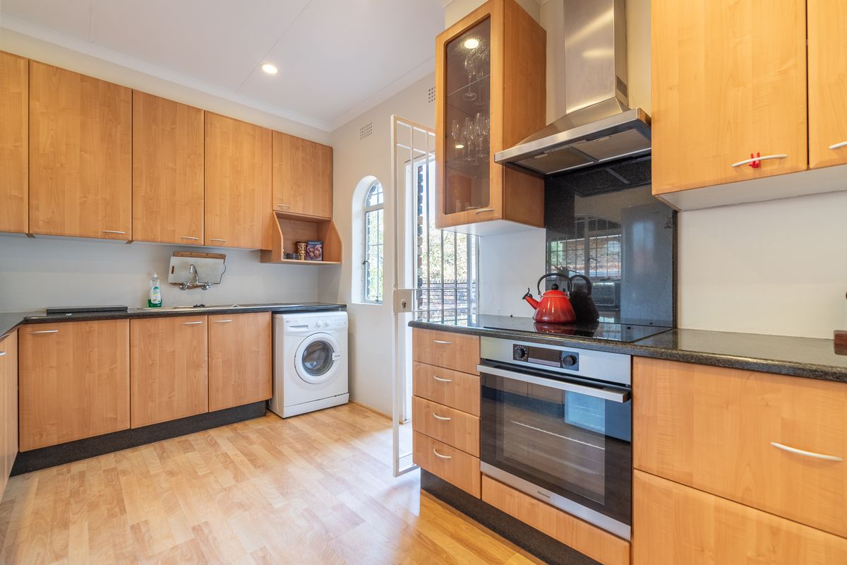 Functional kitchen featuring light wood cabinetry, granite countertops, integrated oven and hob, and direct access to the exterior via a security gate.