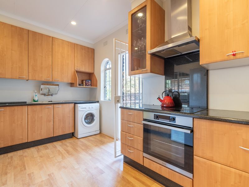 Functional kitchen featuring light wood cabinetry, granite countertops, integrated oven and hob, and direct access to the exterior via a security gate.