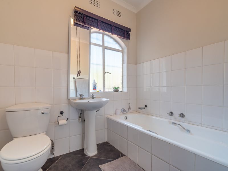 A functional bathroom featuring a pedestal basin, built-in bathtub, toilet, and classic white wall tiling with dark floor tiles.