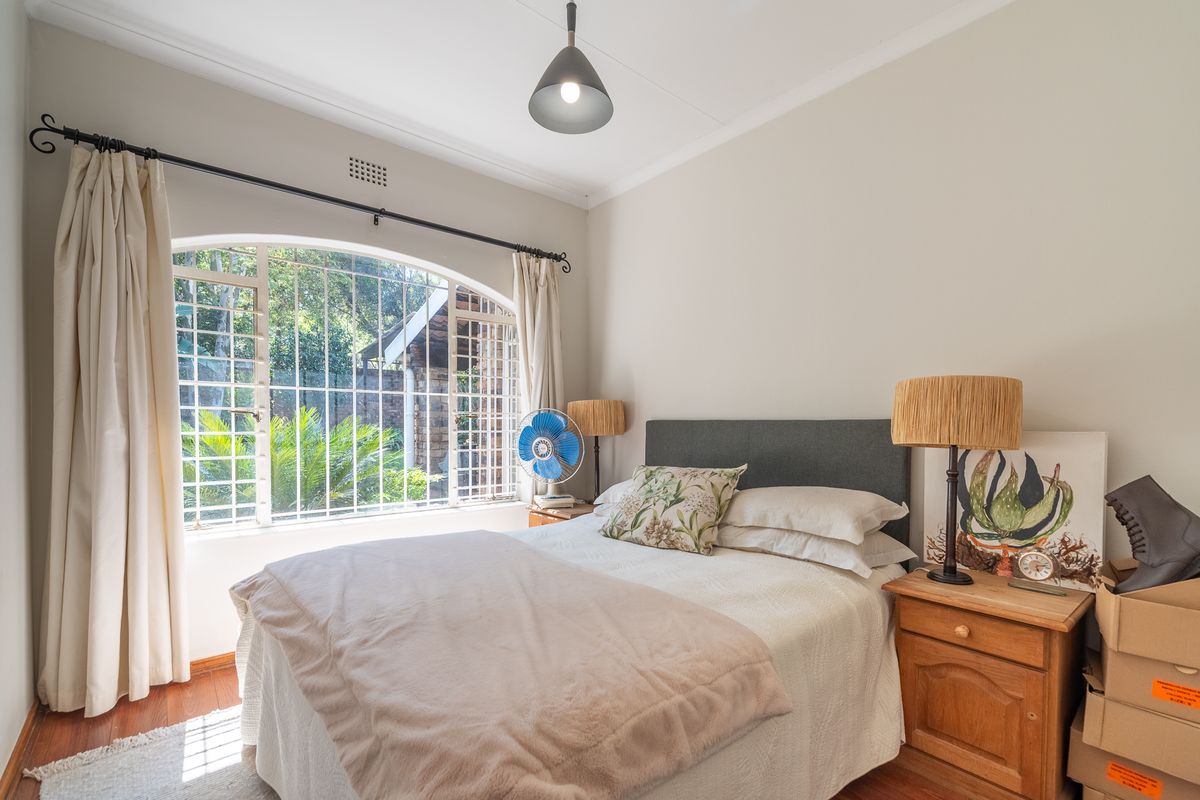 A well-lit bedroom featuring hardwood flooring, an arched window with security bars, and classic cove cornice detailing.