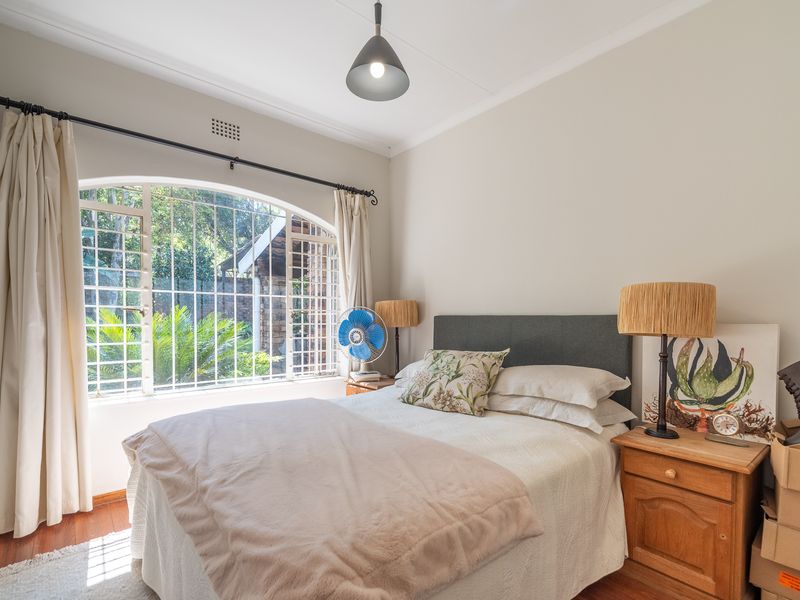 A well-lit bedroom featuring hardwood flooring, an arched window with security bars, and classic cove cornice detailing.