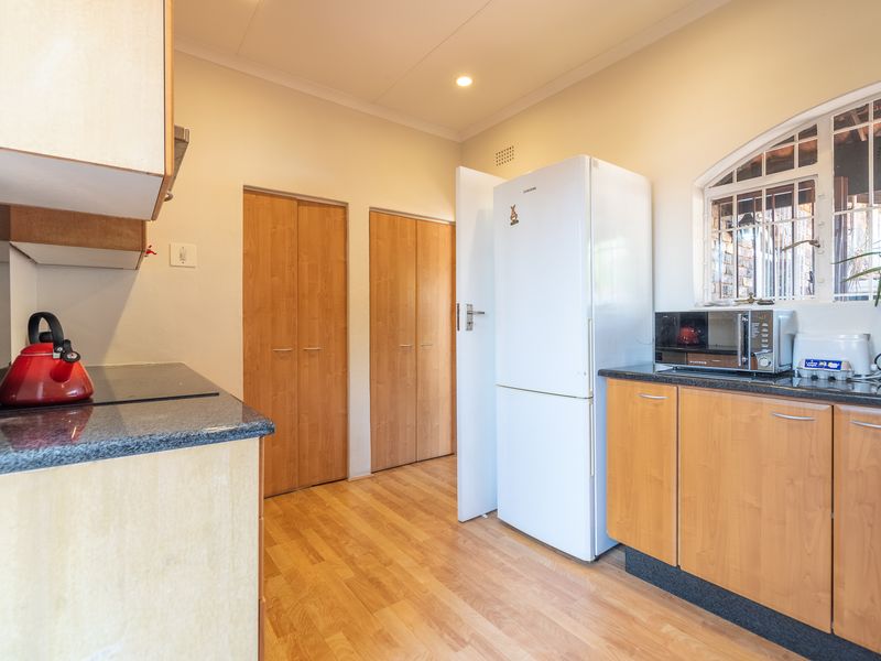 A functional kitchen featuring laminate cabinetry, granite countertops, and wood-look flooring, with built-in storage cupboards and an arched window providing natural light.